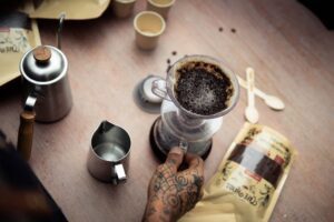 Artistic overhead shot of coffee brewing in a São Paulo café, highlighting tattooed hands and brewing setup.