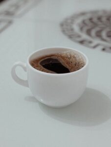 A fresh cup of coffee served in a white cup on a glass table with a subtle background design.