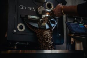 Close-up of coffee beans being roasted in an industrial machine with a hand scooping beans.