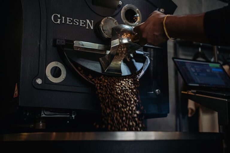 Close-up of coffee beans being roasted in an industrial machine with a hand scooping beans.