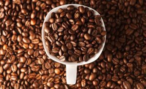 Close-up photo of roasted coffee beans in a mug surrounded by more beans. Ideal for coffee lovers.