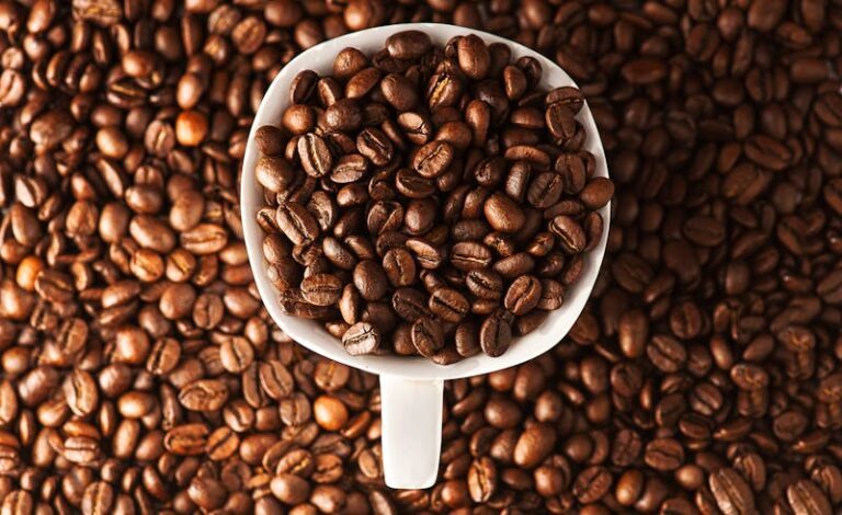 Close-up photo of roasted coffee beans in a mug surrounded by more beans. Ideal for coffee lovers.