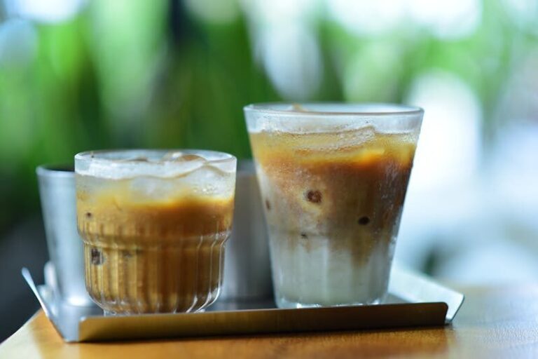 Two glasses of iced coffee placed on a silver tray with a blurred green background.